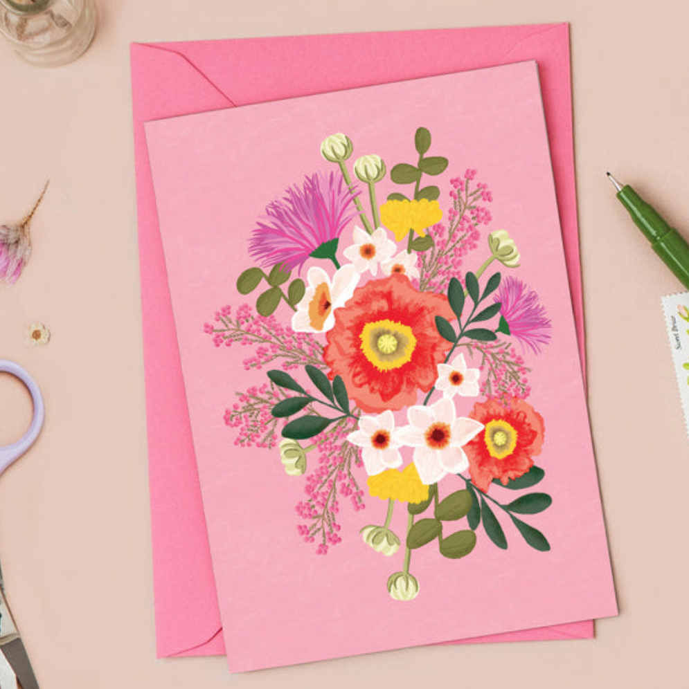 Floral card on a pink envelope with stationery items on a beige background